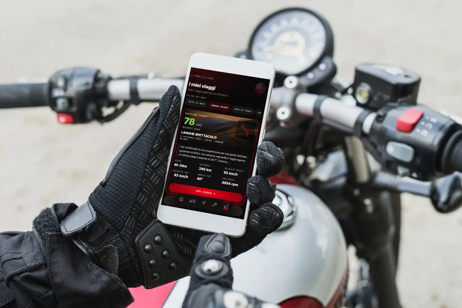 Mano guantata che tiene il telefono con l'app di Mekainos sul manubrio di una moto ferma